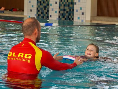 Ein DLRG Rettungsschwimmer bringt einem kleinen Mädchen schwimmen bei